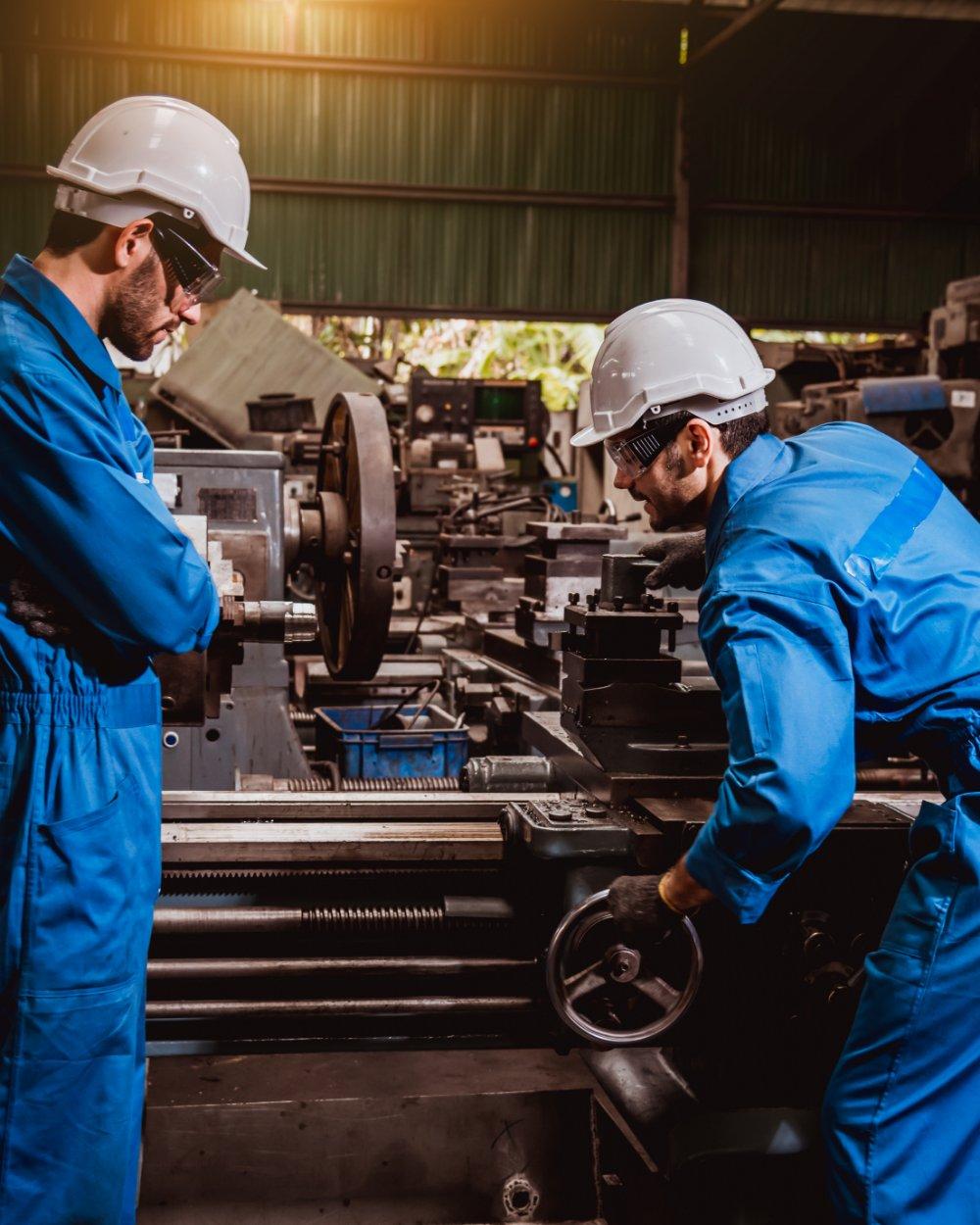 Operários industriais com EPI trabalhando em torno mecânico
